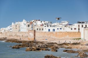 Panoramic view of the UNESCO-listed Medina of Essaouira from the Atlantic coast, featuring historic stone ramparts, rocky shoreline, whitewashed buildings, and the Atlantic Ocean in Morocco.