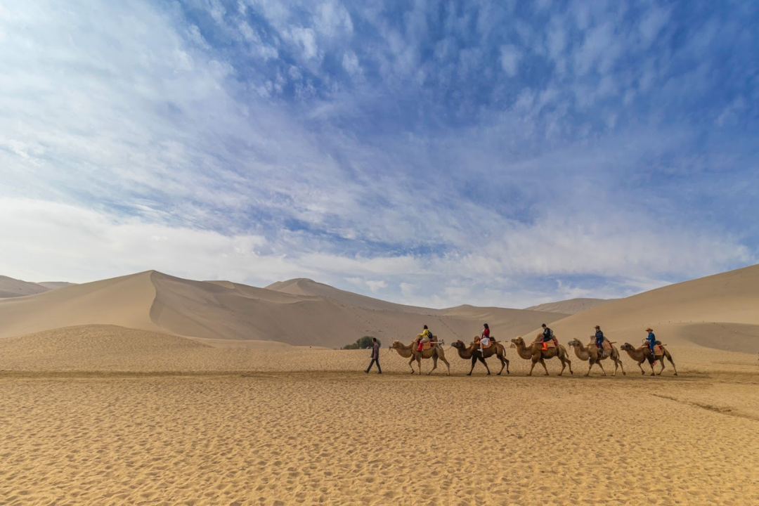Camel caravan crossing the Sahara desert with travelers riding across the dunes