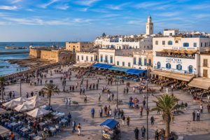 Panoramic view of Moulay Hassan Square in Essaouira featuring lively cafés, the historic Medina, Skala de la Ville, the Atlantic Ocean, and the bustling waterfront in Morocco.