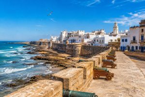 Panoramic view of Skala de la Ville in Essaouira featuring historic stone ramparts, bronze cannons, the Atlantic Ocean, rocky coastline, and the UNESCO-listed Medina in Morocco.