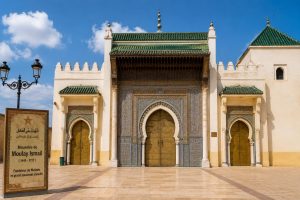 The magnificent entrance of the Mausoleum of Moulay Ismail in Meknes, Morocco, featuring traditional Moroccan zellige tilework, carved cedar wood, and green tiled roofs.